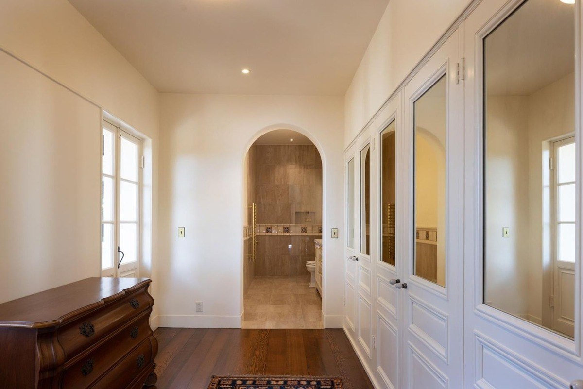 Hallway with a vintage dresser, a tiled bathroom, and a series of doors with mirrored panels.