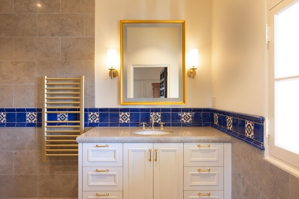 Luxurious bathroom with a single vanity, a heated towel rack, decorative tile work, and a gold-framed mirror.