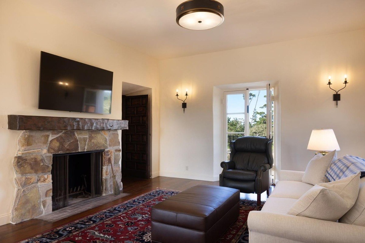 Cozy living room with a fireplace, a flat-screen TV, comfortable seating, and a view of the outdoors.