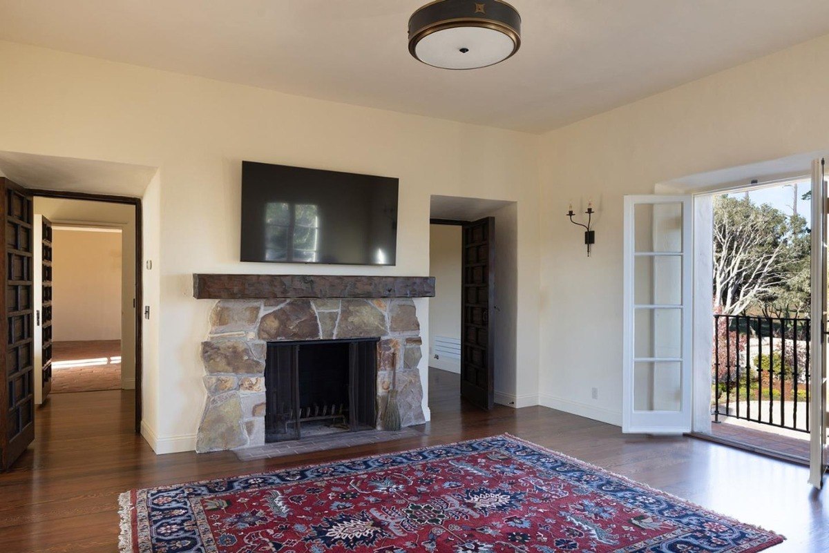 Spacious living room with a stone fireplace, a flat-screen television, and French doors leading to a balcony.