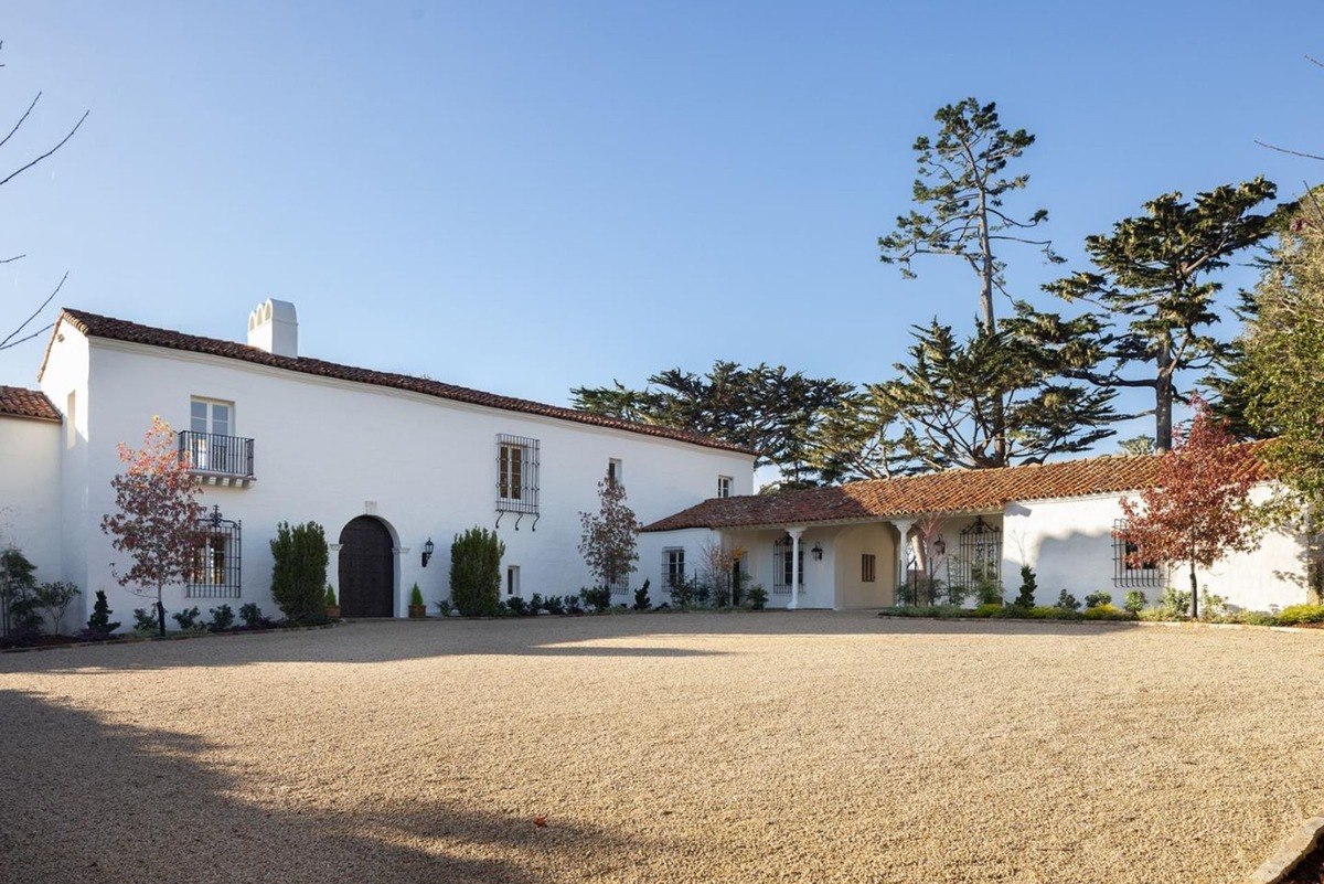 Grand Mediterranean-style estate with a white stucco exterior, terracotta roof tiles, and a large gravel driveway.