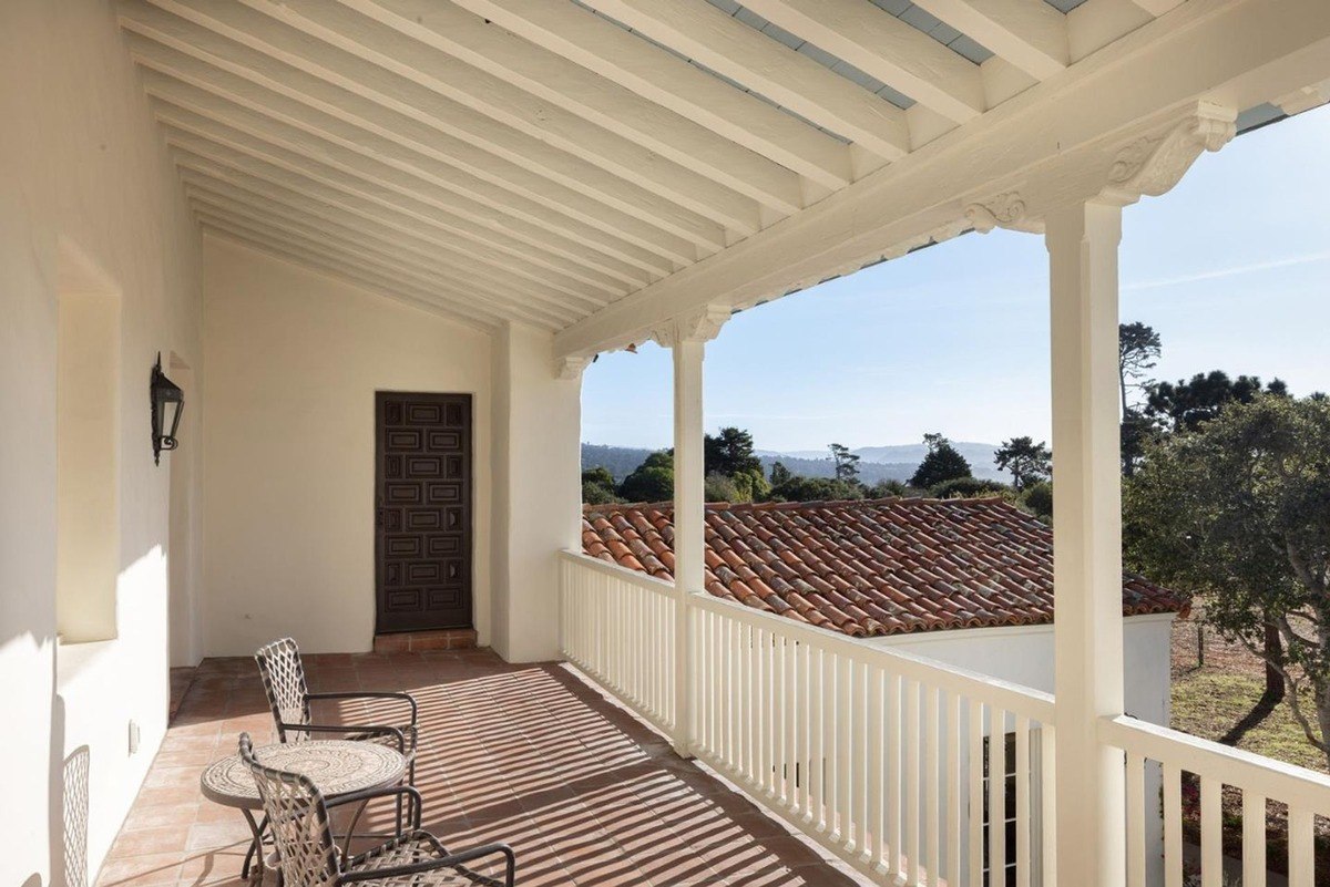 Spacious balcony with a whitewashed ceiling and a wrought iron railing, offering expansive views of the surrounding landscape and a distant coastline.