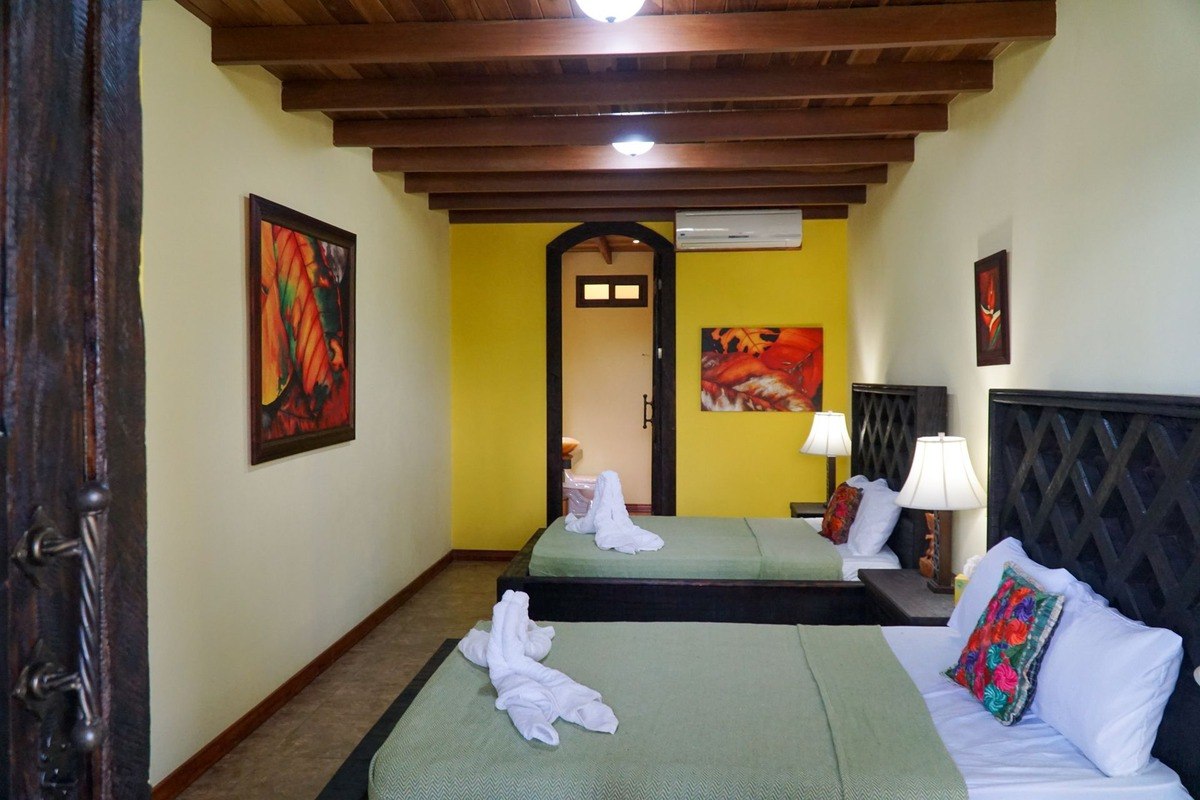 Guest room has two beds, wood ceiling, and artwork.