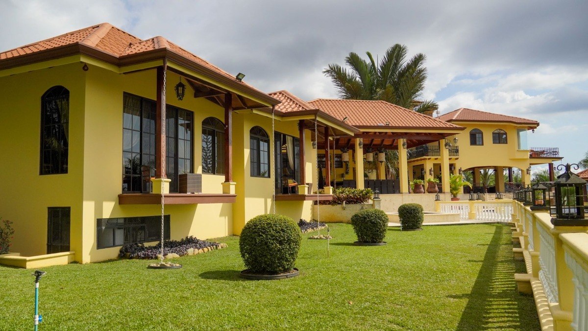 Large yellow house has multiple levels and manicured lawn.