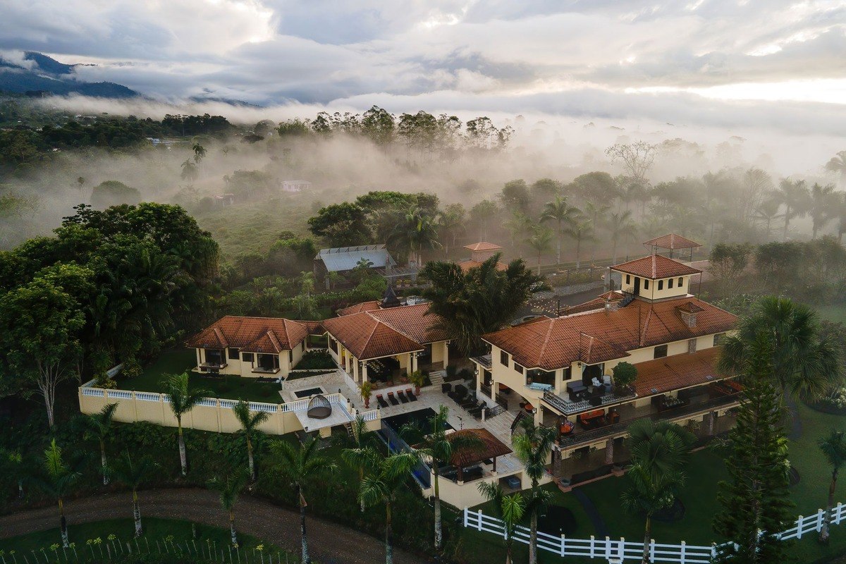 Big house sits on hillside with pool and surrounding fog.