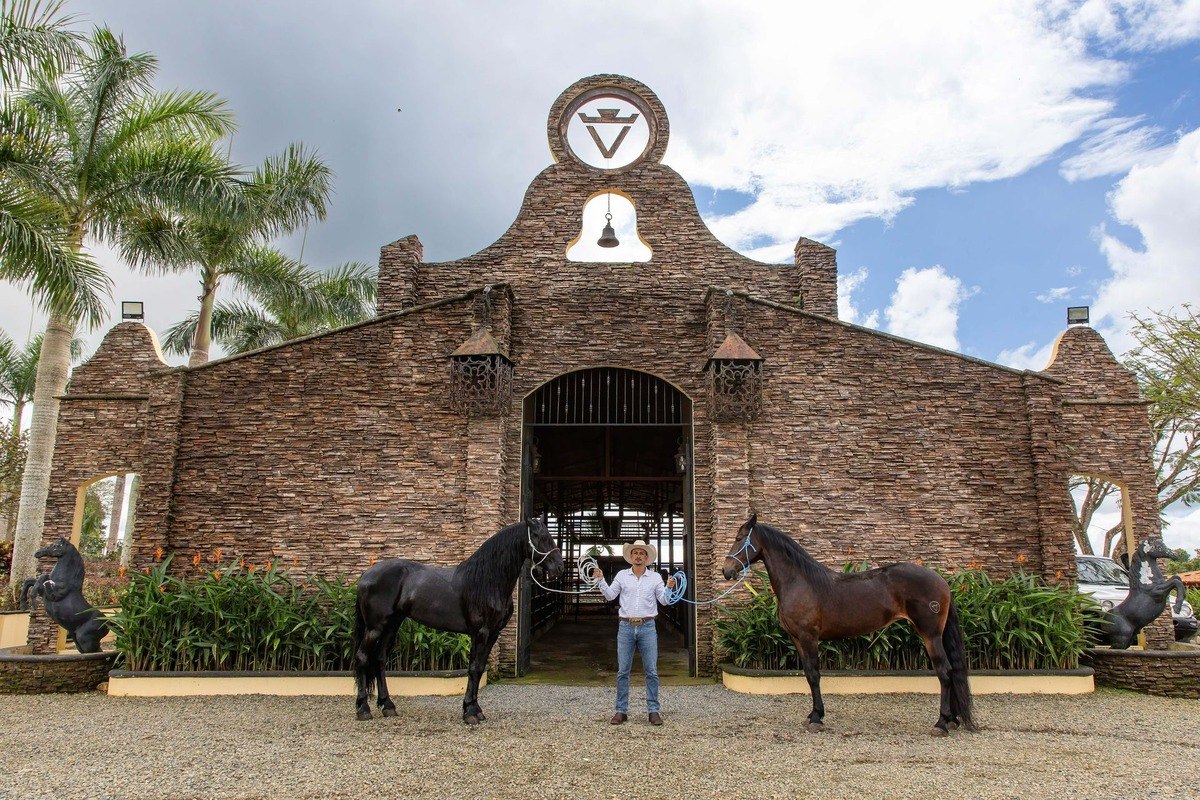 Man stands between two horses in front of stone building.