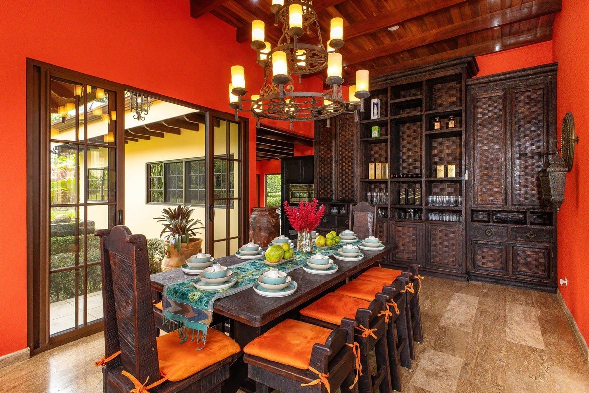 Dining room has orange chairs, wood table, and chandelier.