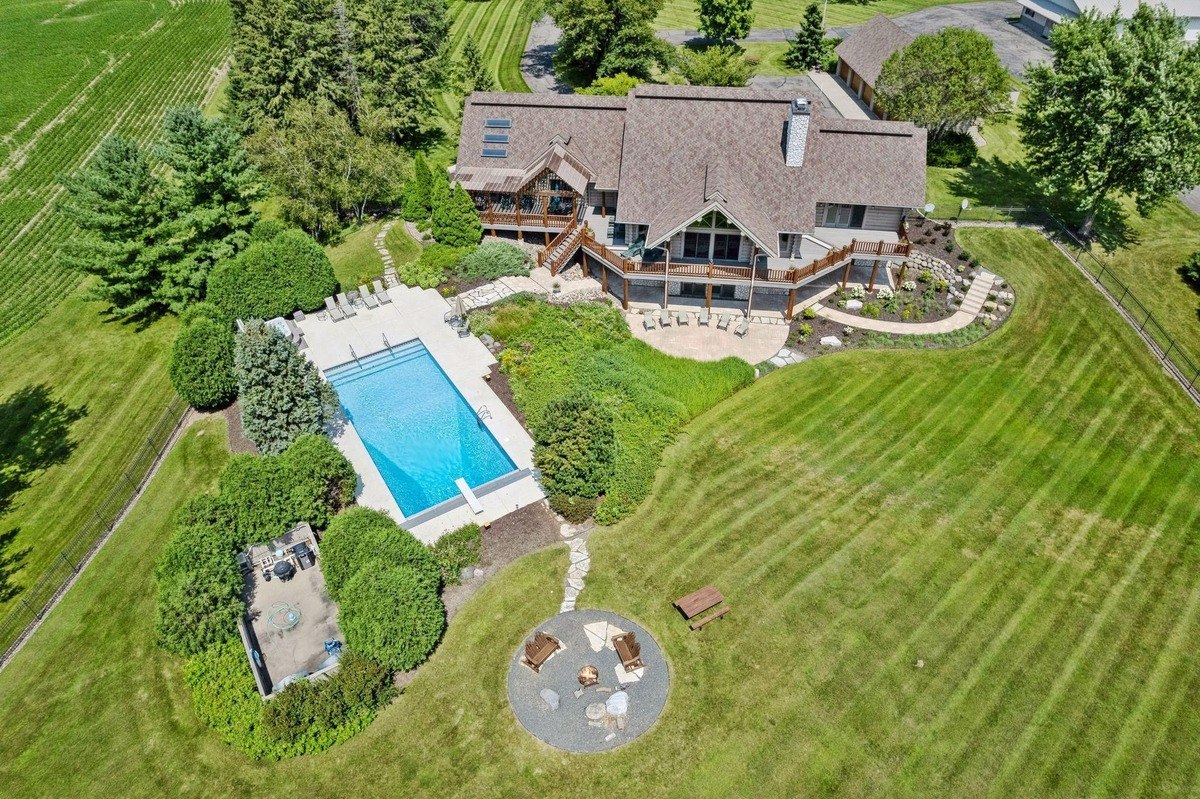 Aerial view of property a large house with a pool, fire pit, and expansive landscaped lawn.