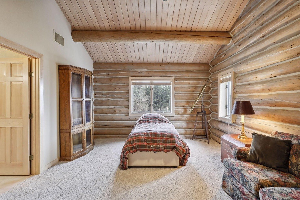 Bedroom a cozy single bed in a room with log walls, a slanted ceiling, and a large window.