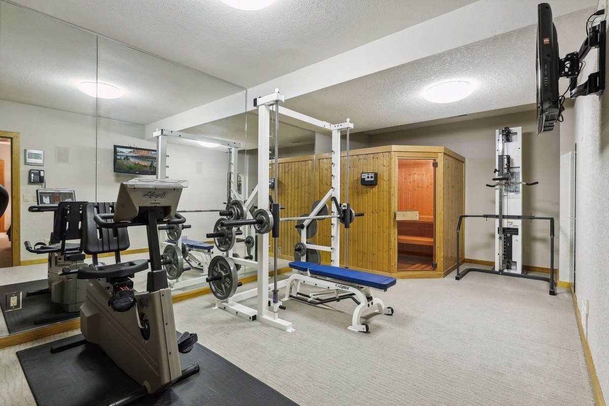 Home a gym area with workout equipment, mirrored walls, and a sauna.