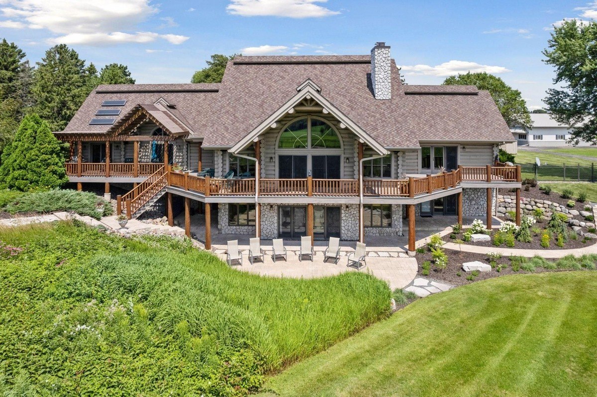 Close-up of the back exterior a log home with a wraparound deck, stone accents, and lounge seating.