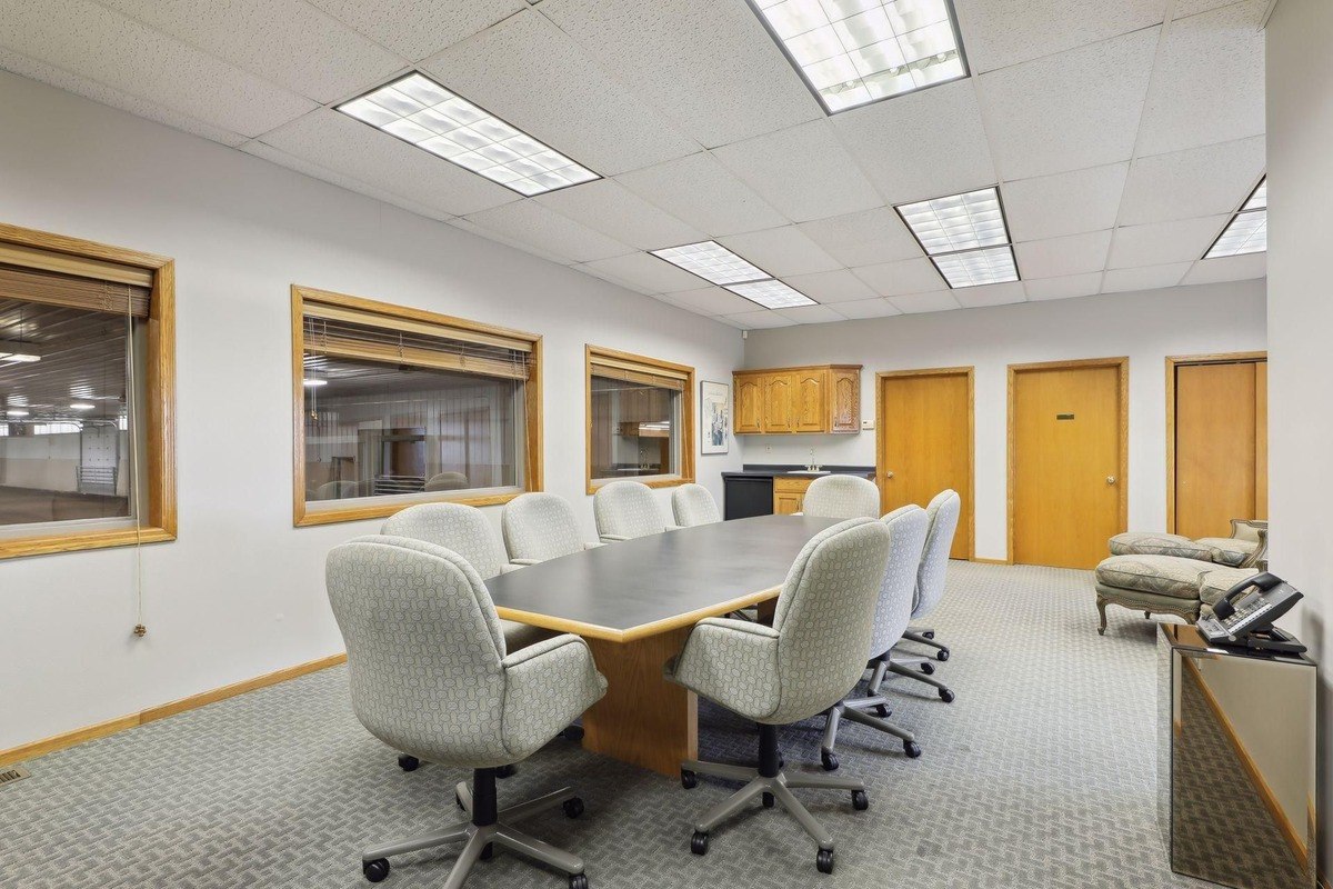 Conference room with a central table and chairs, surrounded by large windows and cabinets.