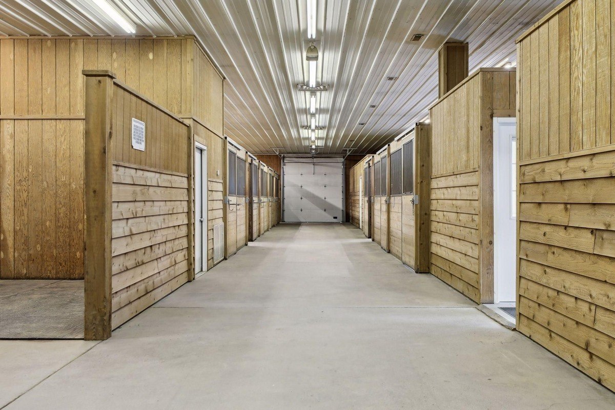 Stable with neatly arranged wooden stalls and a wide central aisle under a high ceiling.