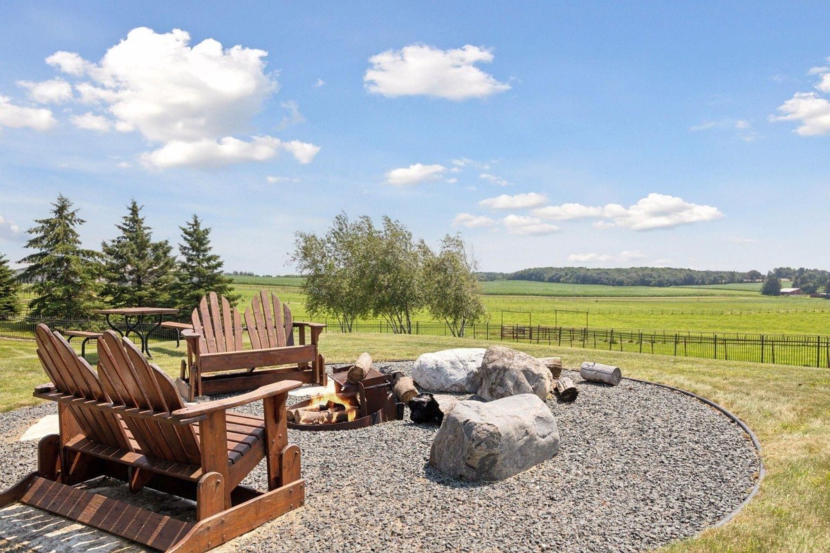 Outdoor fire pit area with wooden Adirondack chairs and a backdrop of lush greenery.