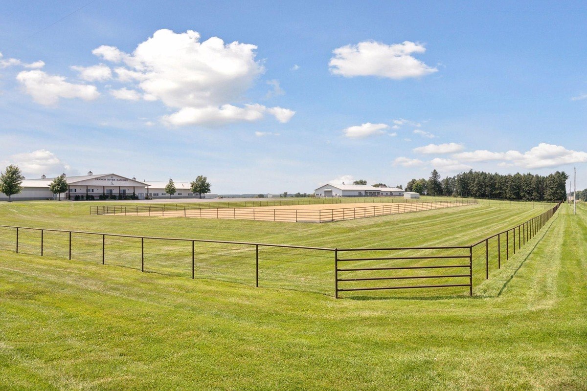 Large outdoor riding arena enclosed by fencing, with adjacent pastures