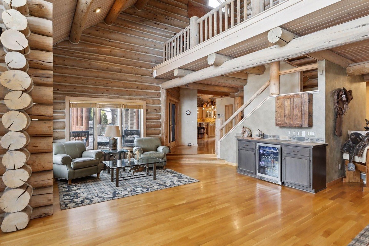 Hallway and living area open space with exposed log beams, a black hutch, and a view of the main living room.