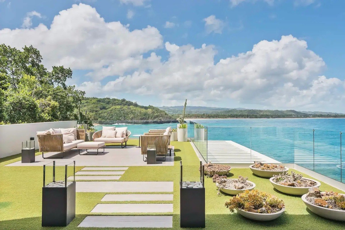 Outdoor patio has modern furniture, artificial grass, and ocean view.