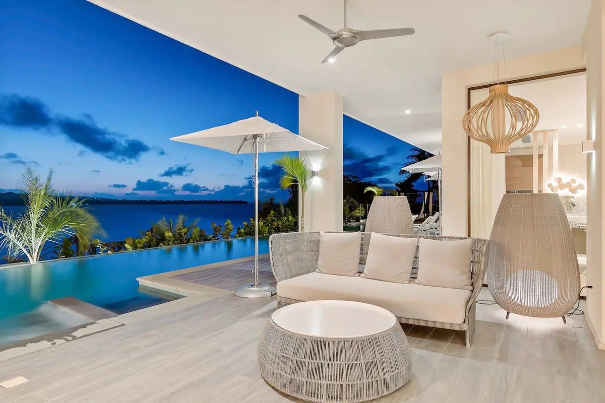 Outdoor lounge area has white wicker sofa, coffee table, and ocean view at dusk.