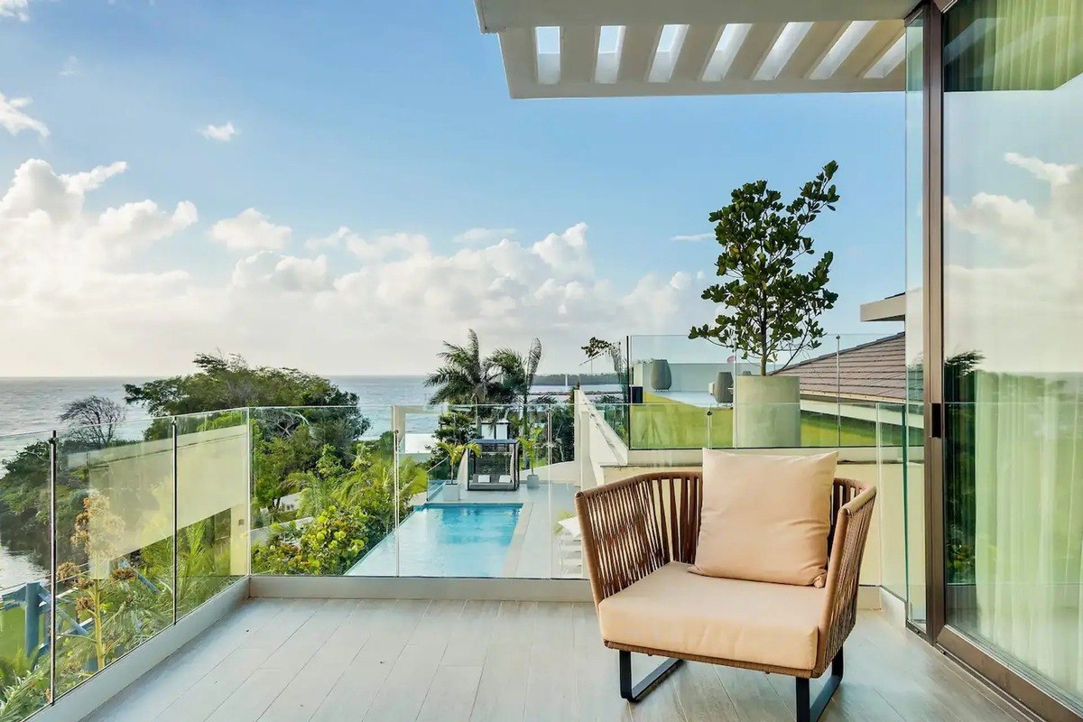 Balcony has wicker chair, glass railing, and ocean view.