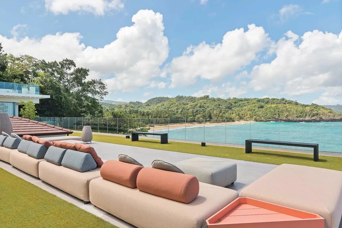 Oceanfront patio has long sectional sofa, artificial grass, and hillside view.