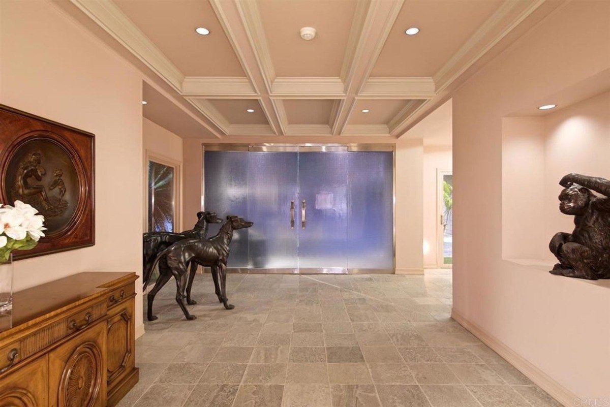 Grand entrance hallway adorned with decorative statues, coffered ceilings, and a frosted glass double door.