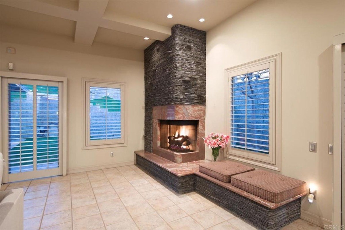 Stone-clad fireplace with a cozy seating area, framed by soft beige walls and shuttered windows.