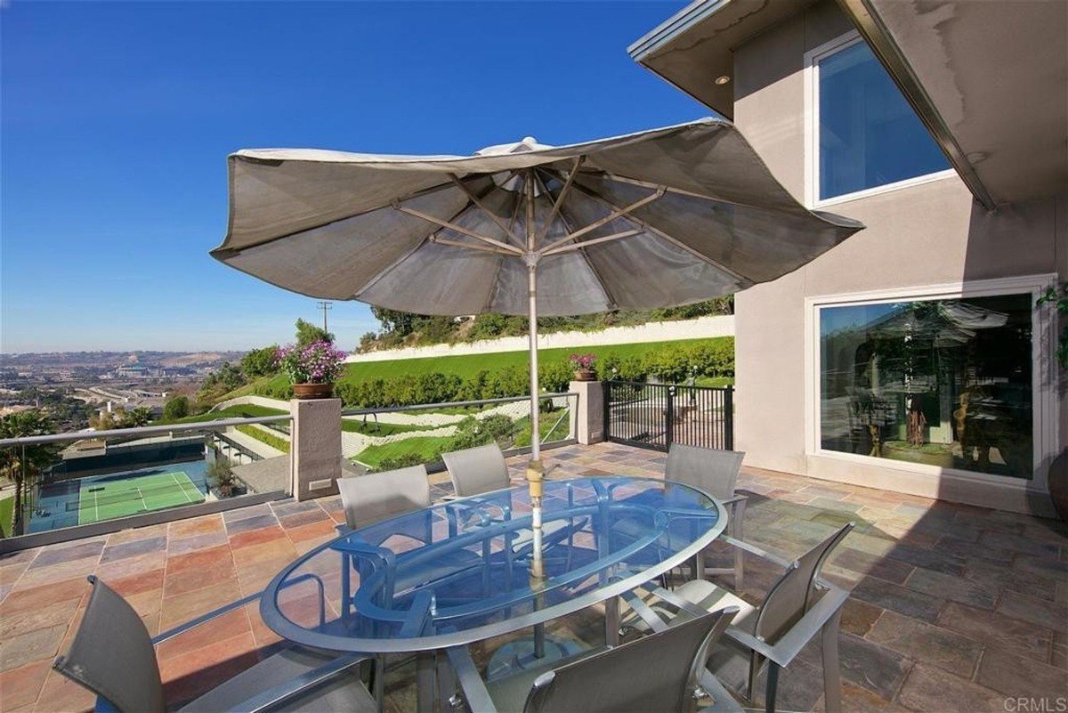 Scenic terrace with a glass dining table, umbrella, and panoramic hillside views.