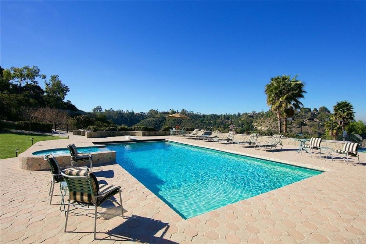 Expansive outdoor pool deck surrounded by lounge chairs and a panoramic hilltop view.