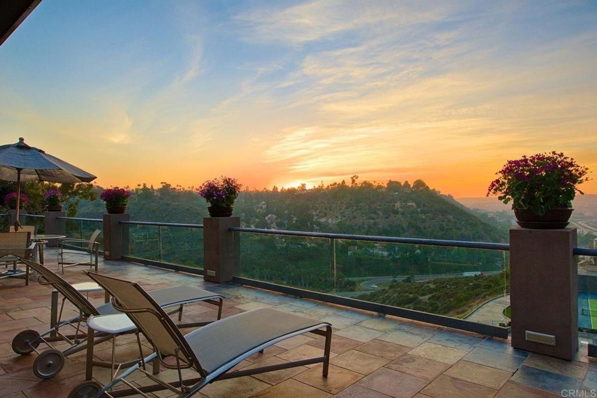 Balcony seating area with lounge chairs overlooking a scenic sunset and hills beyond.