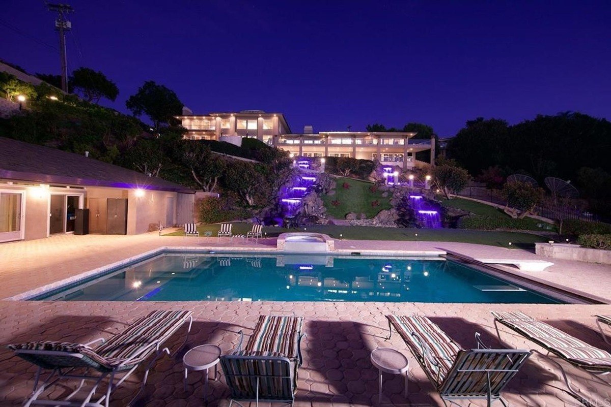 Illuminated pool at night with cascading waterfalls and vibrant purple lighting enhancing the surrounding garden.