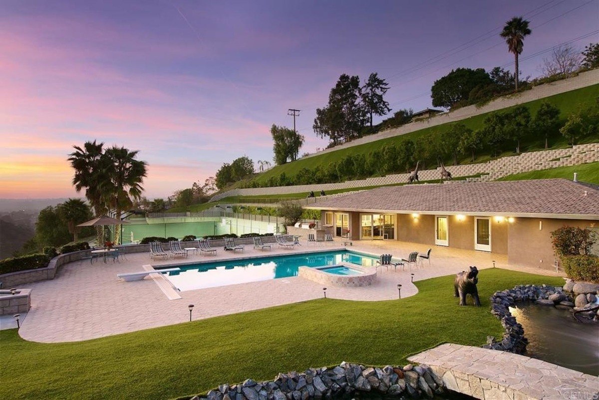 Outdoor pool space includes lounge chairs, lush grass, and a scenic landscape illuminated by sunset colors.