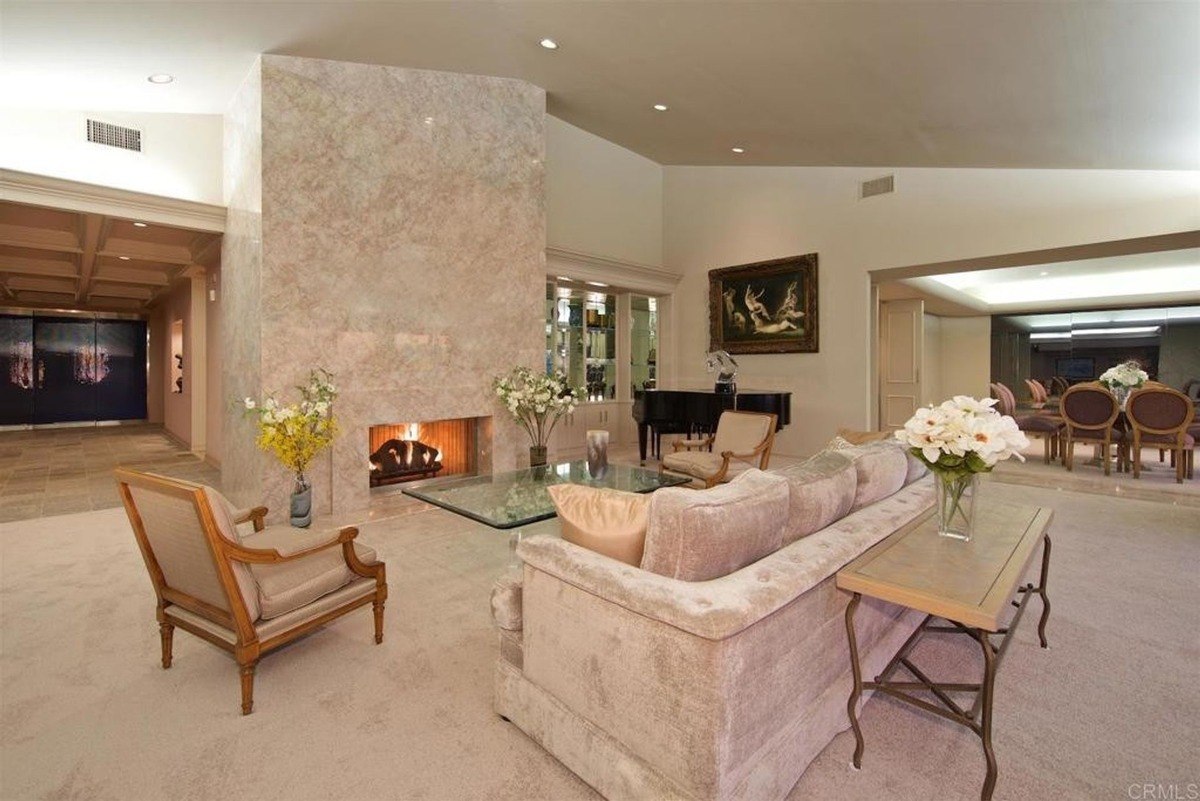 Formal dining area with a glass-top table, upholstered chairs, and floor-to-ceiling windows offering scenic views of the sunset.