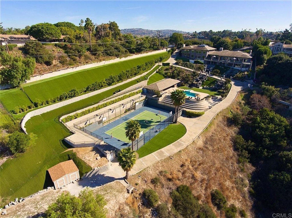 Aerial view captures the tennis court, pool area, and the layout of the hillside mansion surrounded by landscaped greenery.