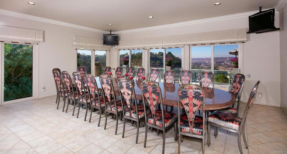 Meeting or dining room with a long table, patterned chairs, and wraparound windows overlooking the surrounding hills.