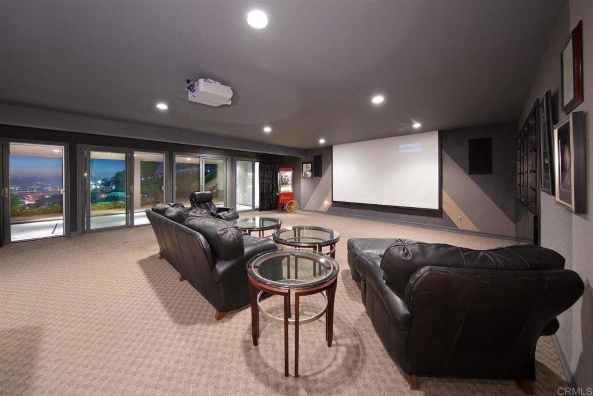 Home theater room equipped with a projector, black leather seating, and glass walls showcasing exterior views.