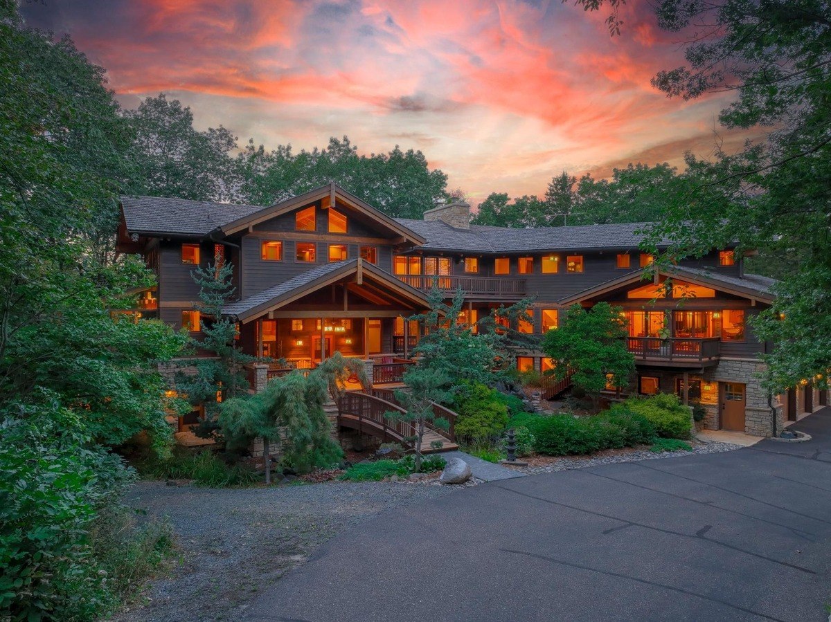 Grand, multi-level home with a stone exterior and multiple balconies is illuminated by a vibrant sunset, creating a picturesque and inviting scene.