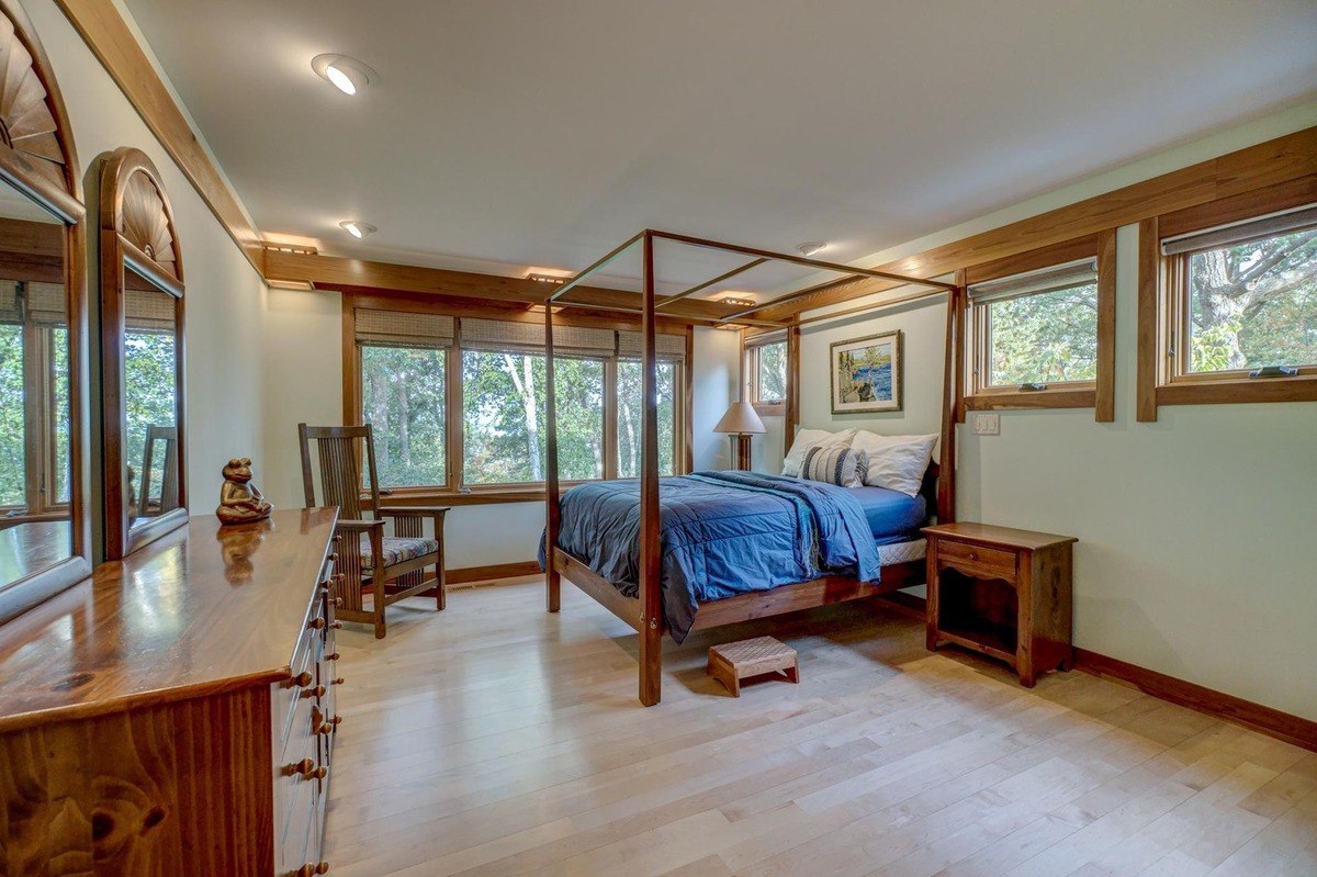 Tranquil bedroom with a four-poster bed, large windows offering views of the outdoors, and a warm wood aesthetic creates a relaxing retreat.