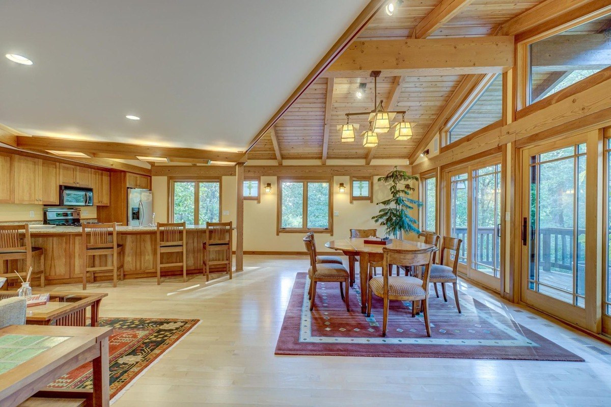 Natural light floods this open-concept living space, showcasing a kitchen, dining area, and living room connected by a vaulted ceiling and hardwood floors.