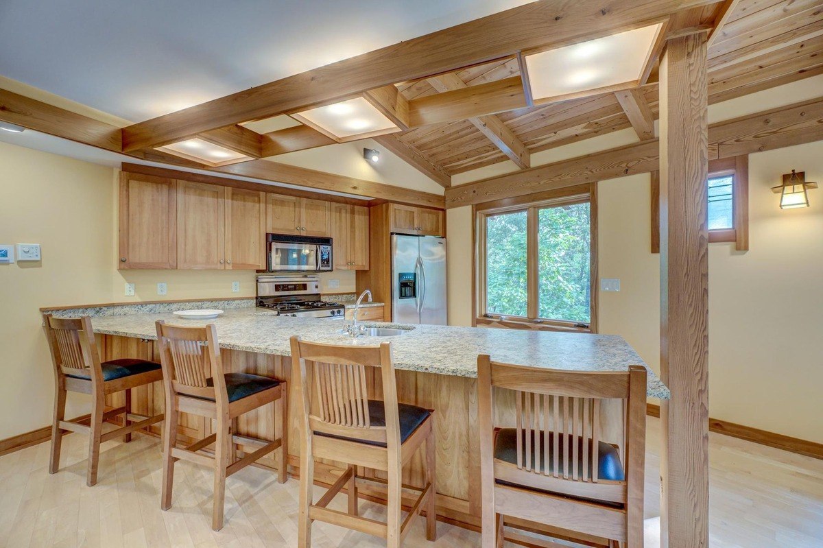 Warm and inviting kitchen features a long breakfast bar, wood cabinetry, and a vaulted ceiling with exposed beams.