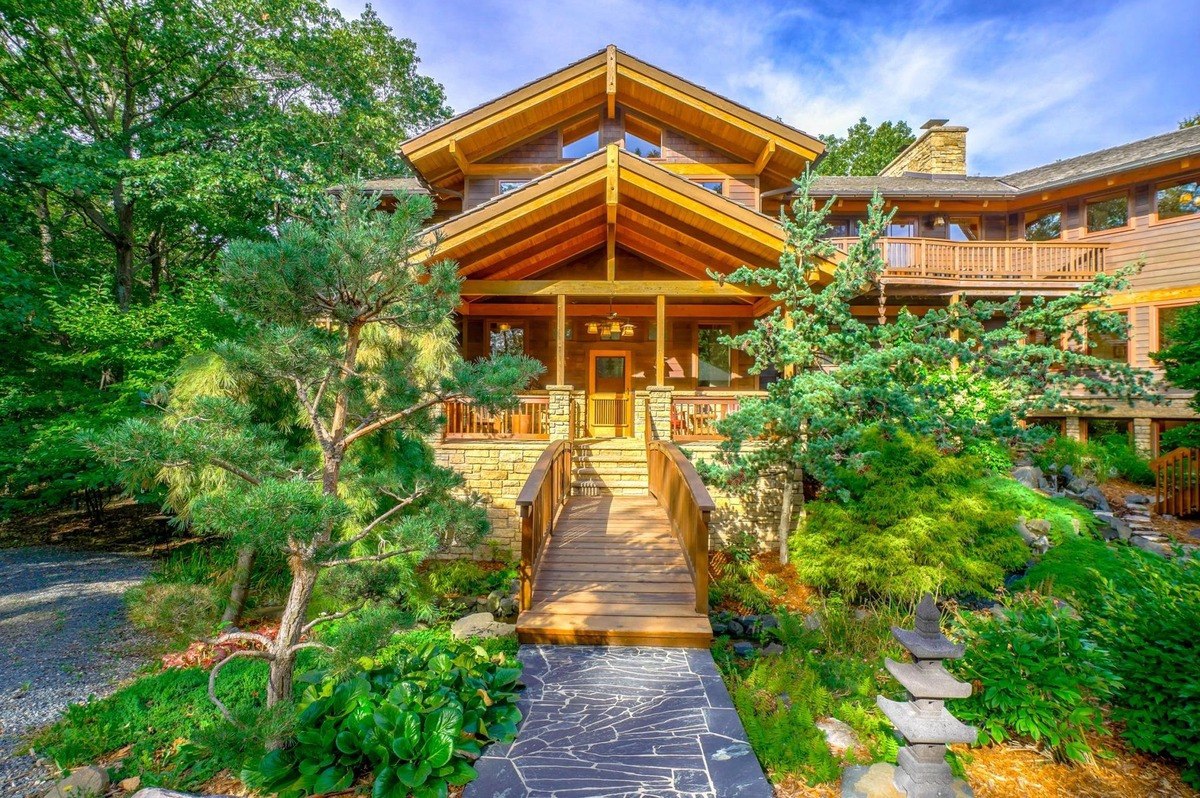 Wood-sided home with a stone foundation features a picturesque entrance with a small bridge and a beautifully landscaped garden.