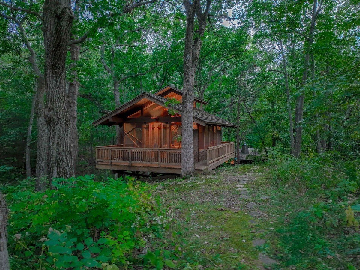 Cabin nestled amidst towering trees offers a secluded retreat with a warm glow emanating from its windows.