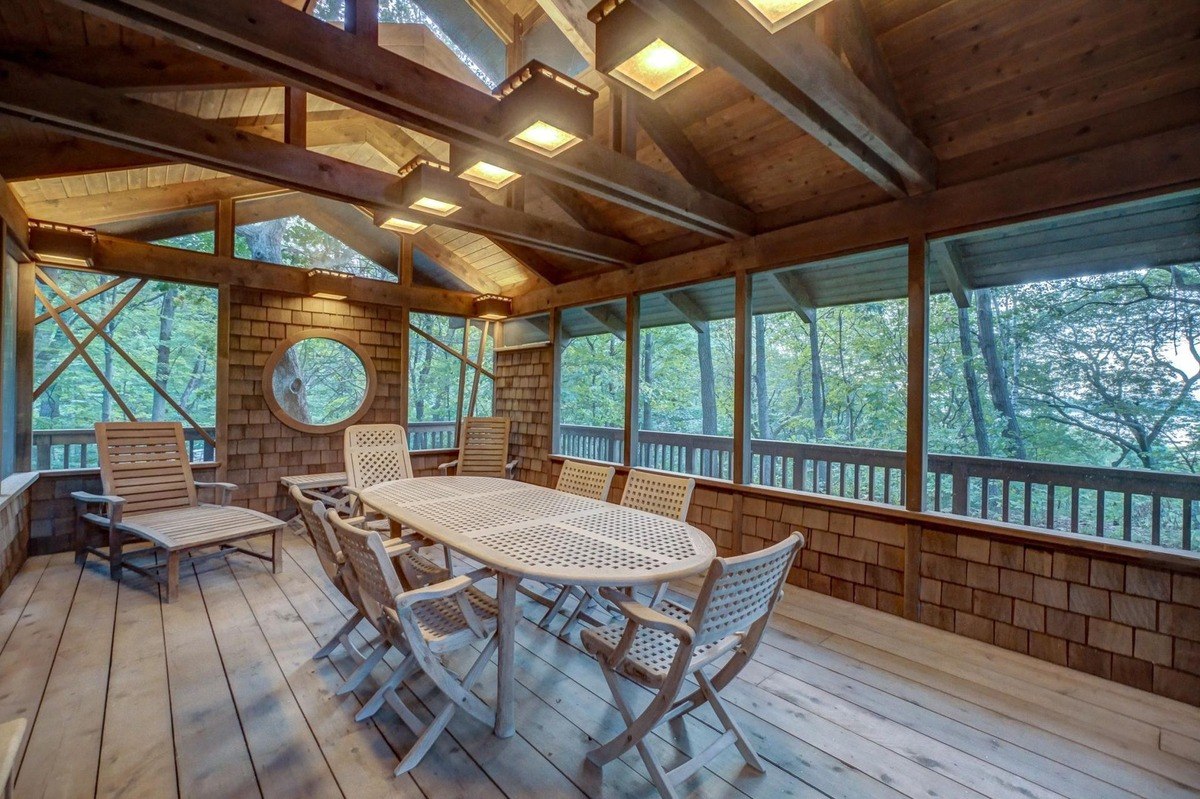 Screened-in porch with a vaulted ceiling and large windows offers a peaceful outdoor retreat, featuring a dining table and comfortable seating.