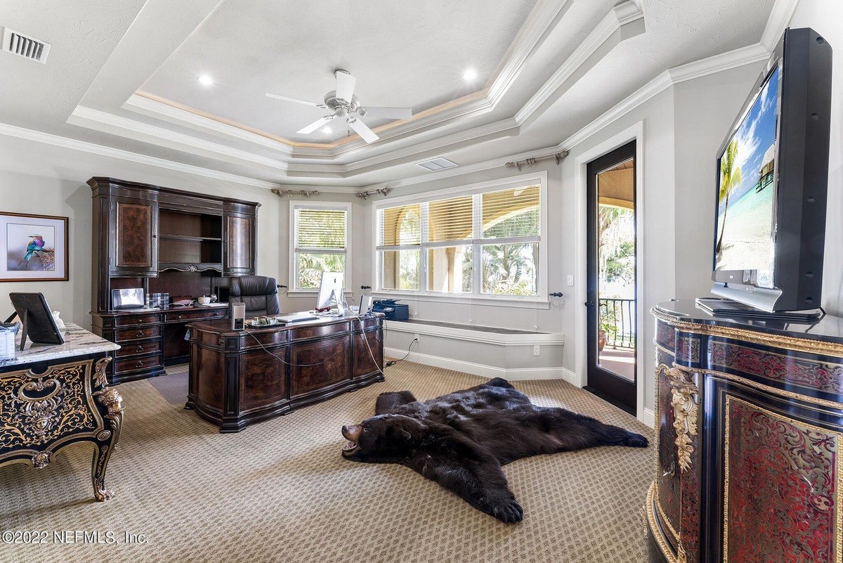 Home office features large windows, dark wood furniture, and a bear rug on the floor.