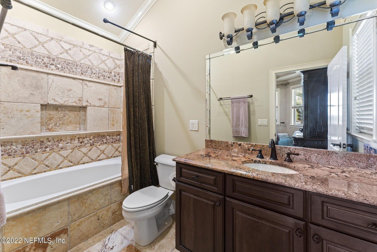 Bathroom has granite countertop, dark wood cabinets, and a shower/tub combo.