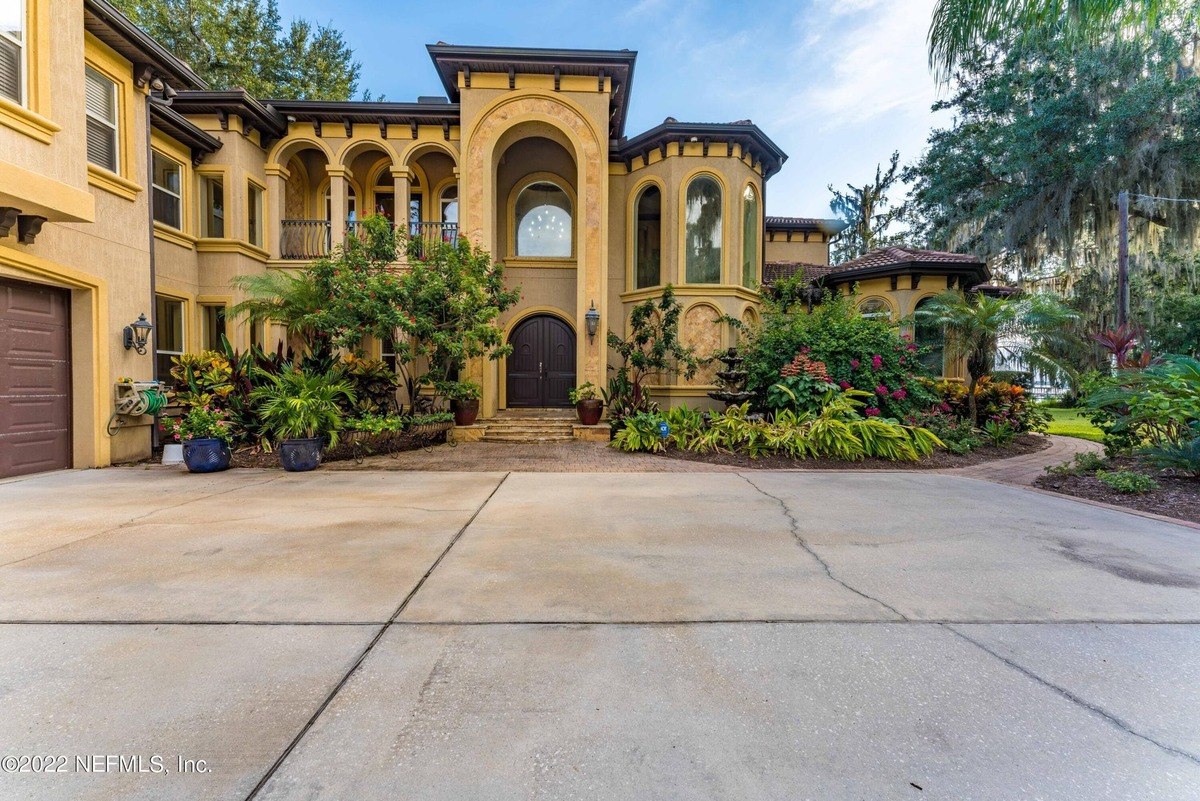 Large, tan house with arched entryway and landscaping is shown.