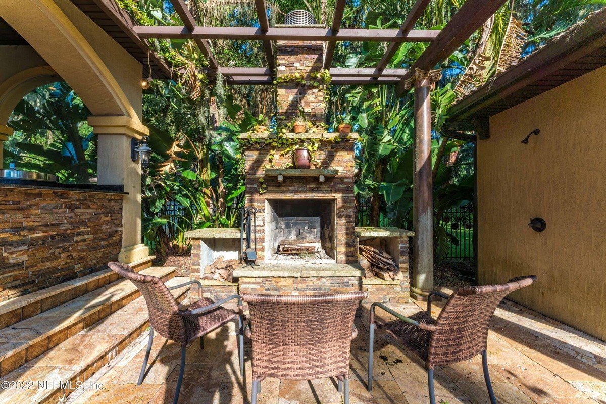 Outdoor patio features a stone fireplace, pergola, and wicker chairs.