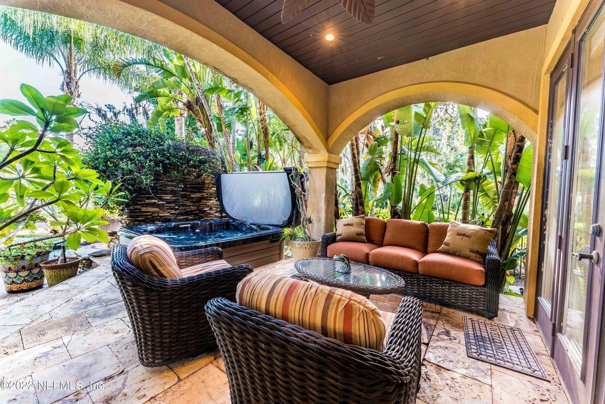 Patio has wicker furniture, hot tub, and lush tropical landscaping.