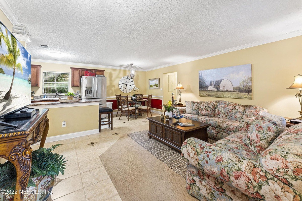 Living room has floral couch, coffee table, and a view of kitchen and dining area.