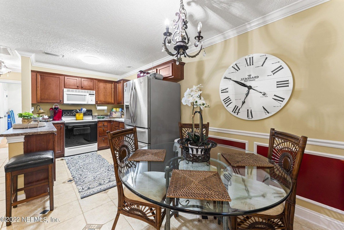 Kitchen and dining area feature wood cabinets, a glass table, and a large clock.