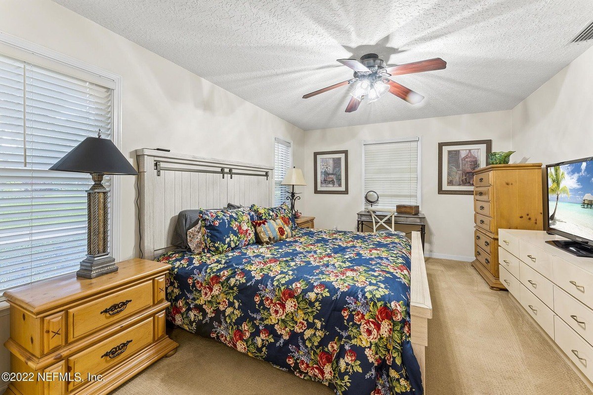 Master bedroom has a floral comforter, ceiling fan, and a dresser with a TV.